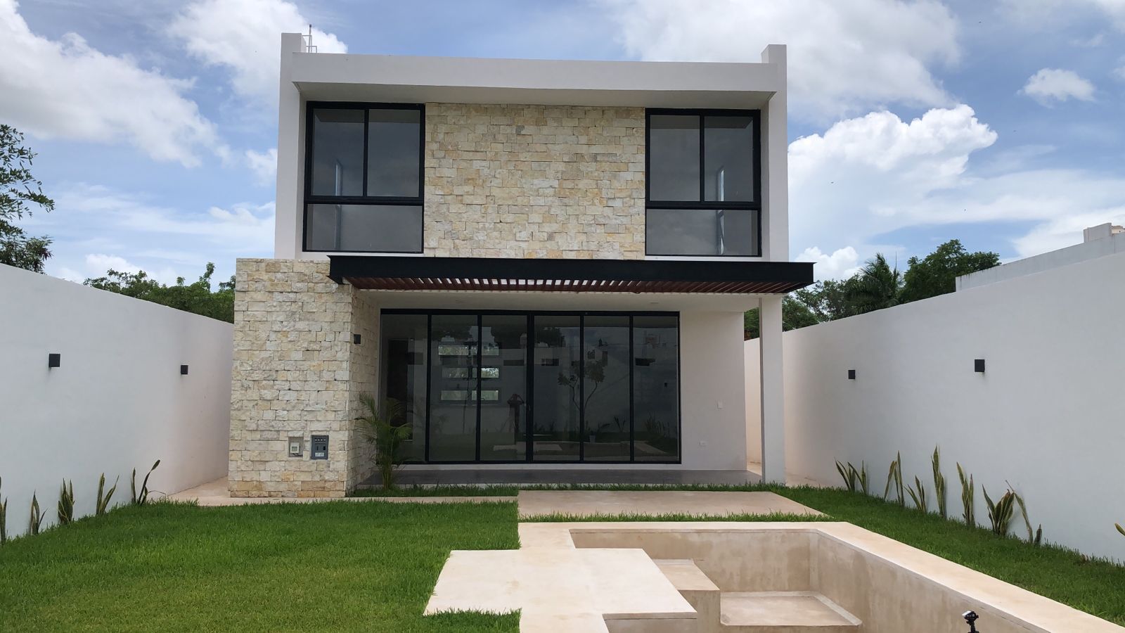 Fachada posterior de Arbórea 290 con muro de piedra crema maya, pérgola y jardín